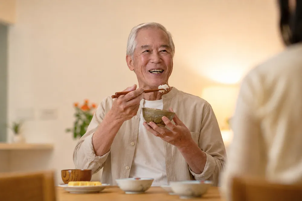 一位年長長輩擁有健康、整齊的牙齒，正開心且順暢地享受美食進餐。畫面傳達出透過 Pro Arch 一日全口重建後，成功擺脫全口缺牙與活動假牙的困擾，當日即刻恢復牙齒外觀與咀嚼功能，重拾品嚐美食的幸福生活品質。